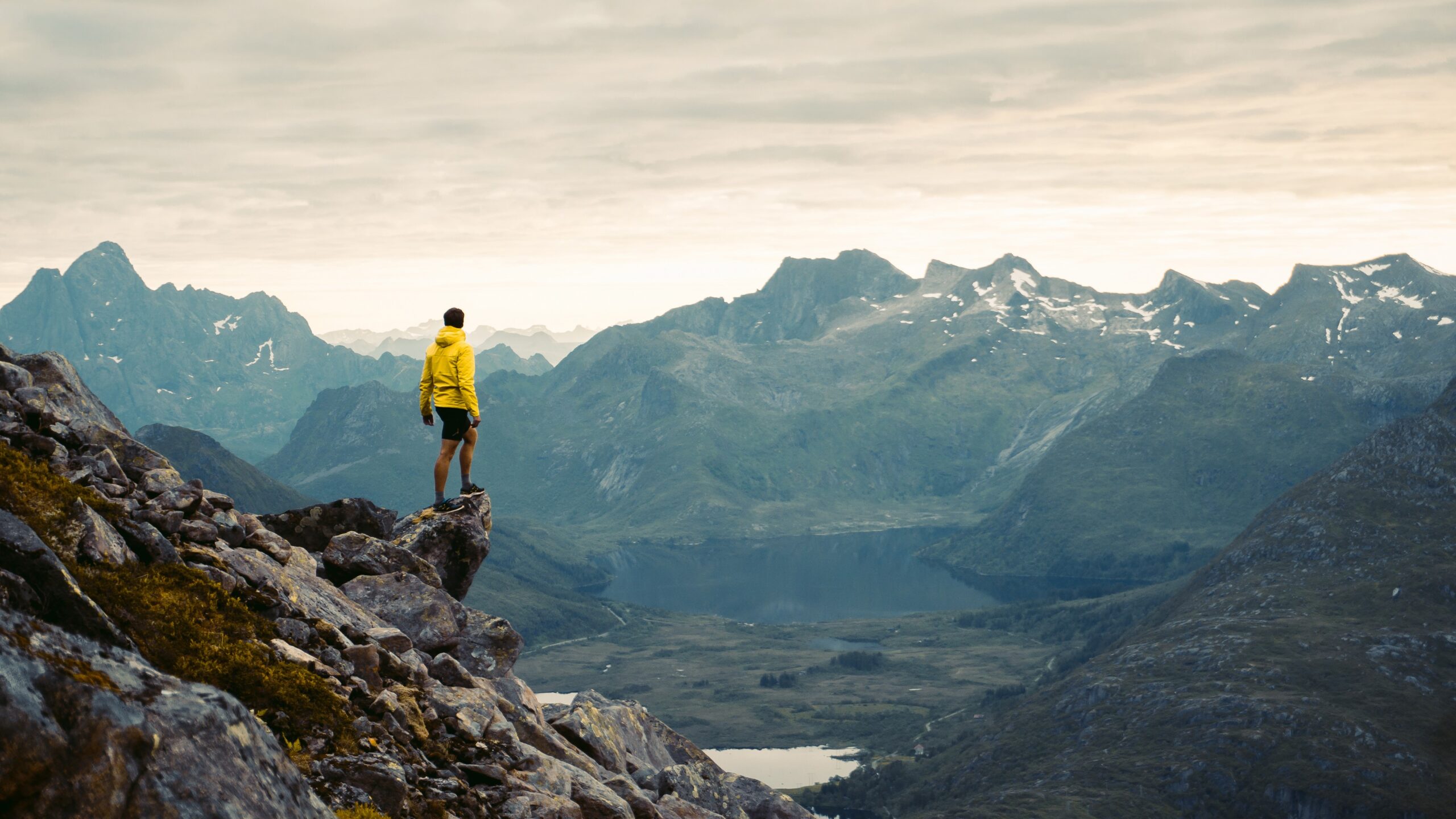 Picture of a man in a yellow jacket standing on a mountain looking out over a mountain landscape